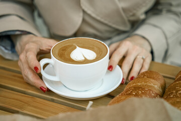 Hands holding a cup of coffee and baguettes on a wooden table.