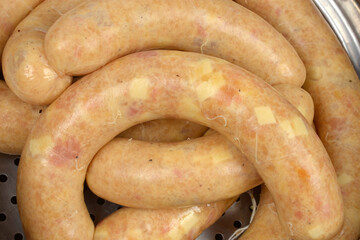A close-up shows several raw, homemade chicken sausages with visible cheese pieces lying curled in a metal steaming pot insert