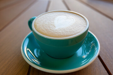 A teal ceramic cup with heart-shaped latte art 