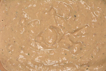 An extreme close-up captures the thick, creamy, beige-brown texture of a homemade chicken liver pate, showing swirls and small visible pieces of herbs or seasoning
