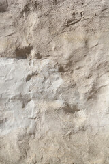 A vertical close-up shot of a heavily textured, uneven wall surface covered in rough, patchy light beige stucco