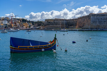 Covered Luzzu in Front of Grand Harbour Bastions and Cloudy Blue Sky