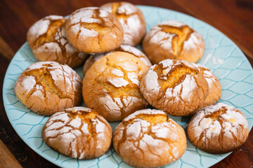 Golden, cracked cookies dusted with powdered sugar rest invitingly on a patterned blue ceramic plate.