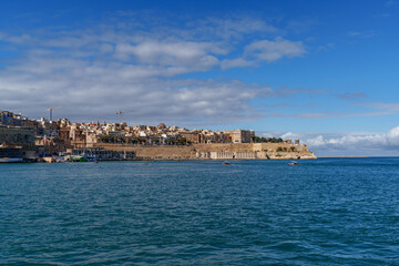 Obraz premium Fortified Peninsula and Waterfront Promenade across Calm Blue Bay under Patchy Clouds