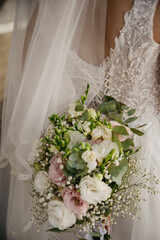 On the wedding day, the bride in a white modern dress with a long veil holds a large bouquet of roses in her hands, showing off her back