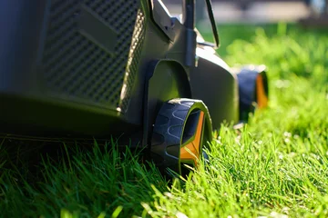 Fotobehang Lime groen Electric lawnmower standing on green grass in backyard near residential house. Concept of lawn care, gardening, landscaping and suburban home maintenance  © Lazy_Bear