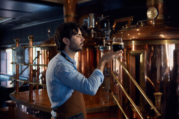 A man is holding a cold glass of beer inside a local brewery