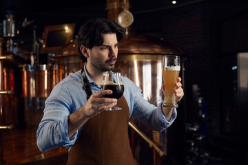 A man in a kitchen apron is holding two glasses filled with beer