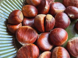 Close up of fresh raw chestnuts arranged on a green ceramic plate