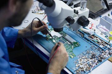 Electronics repair technician working under microscope