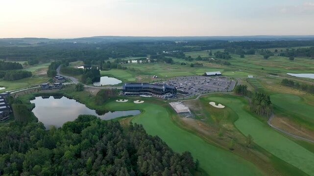 A stunning aerial drone shot orbiting the TPC Toronto at Osprey Valley golf course in Caledon, Ontario, during the golden hour, showcasing its modern clubhouse and pristine fairways.