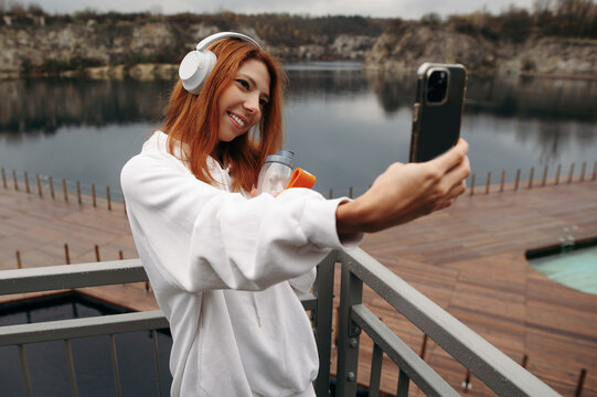 Woman wearing headphones taking selfie on balcony lake