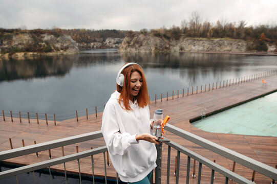 Woman with headphones standing on balcony overlooking deep lake