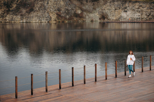 Woman walking wooden pier near big lake after sport looking distance