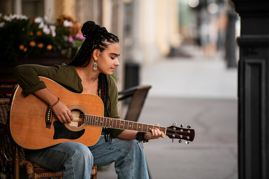 girl with pigtails plays acoustic guitar while sitting on street