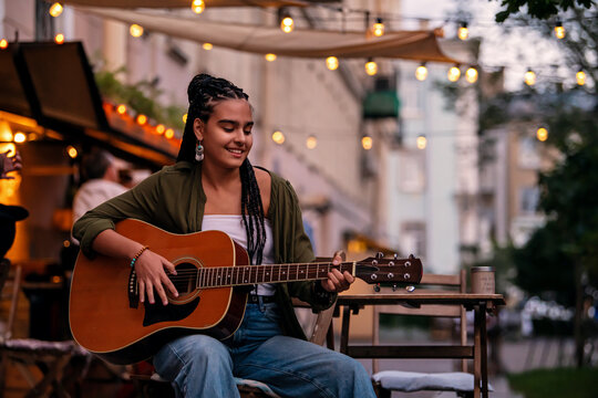 girl musician plays guitar on an evening street at a summer cafe.