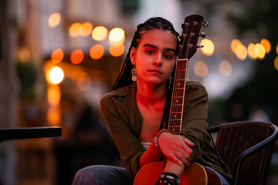 teenager with braids plays an acoustic guitar on an evening street.