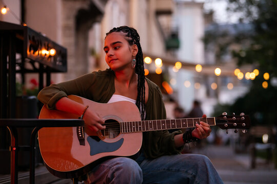 girl musician plays guitar on an evening street at a summer cafe.