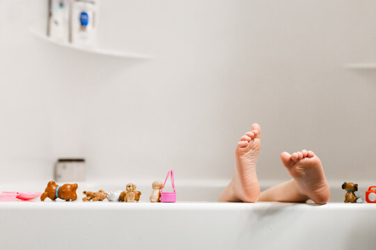 Child's feet on bathtub ledge surrounded by bath toys