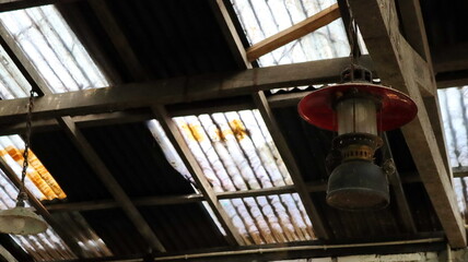 Obraz premium Old lantern hangs from the wooden beams of a dilapidated warehouse ceiling, casting a dim light in the industrial space, creating a nostalgic atmosphere.