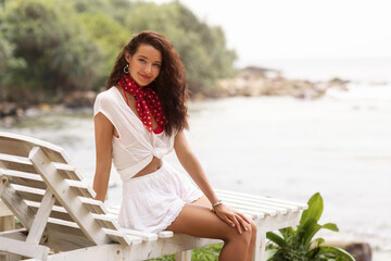 Smiling Woman in White Summer Outfit Relaxing on Lounge Chair by the Ocean