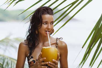 Tanned Woman Holding Coconut On Tropical Beach Under Palm Leaves © Buyanskyy Production