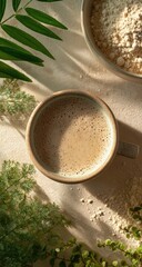 Light-brown coffee drink in a beige mug, surrounded by plants and powder