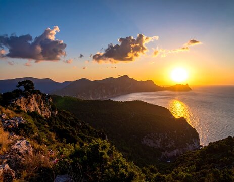 Vivid sunset over coastal mountains, silhouetting a rocky promontory and vegetation in a panoramic, scenic view