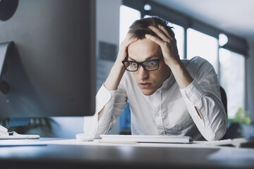 Insane stressed office worker sitting at desk with head in hands