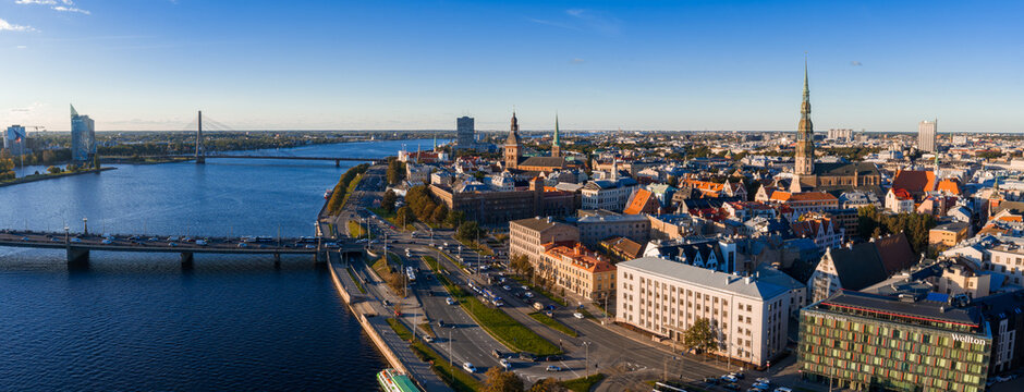 Aerial view of Riga, Latvia, featuring the Daugava River, St. Peter's Church spire, National Library, Latvian flag, and historic Old Town architecture.