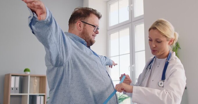 Clinician helps an overweight fat patient in a clinic exam, using tape to record waist measurement and provide obesity counseling on diet and health risks. Nutritionist measures patient waist
