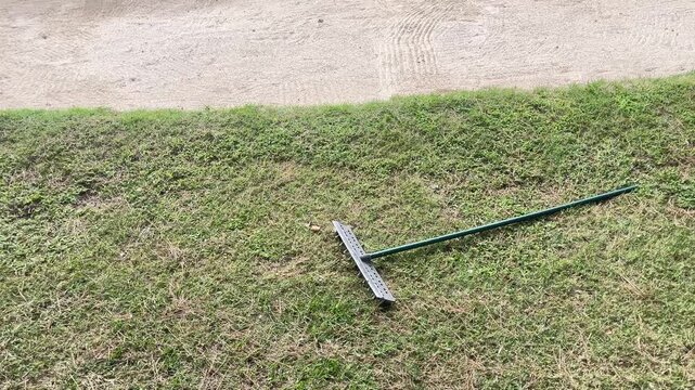 A green lawn mower is sitting on a patch of dry grass. The grass is brown and dry, and the mower is leaning against the ground. The scene gives off a sense of neglect and abandonment