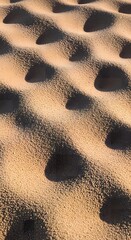 Hypnotic repeating pattern of deep circular pits in golden desert sand with dramatic shadows