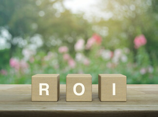 ROI acronym letter on wood block cubes on wooden table over blur pink flower and tree in park, Return on investment concept