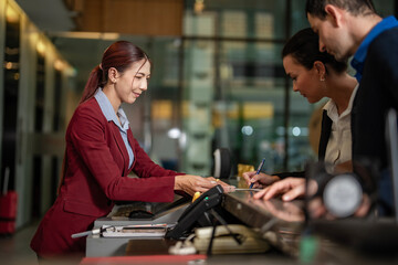 Professional woman at hotel reception desk helping guests sign documents for check-in. Represents hospitality, tourism, and business travel.