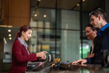 Travelers checking in at hotel counter with staff providing customer service. Ideal for travel, hospitality, and accommodation marketing.