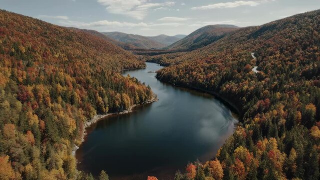 Aerial view shows a lake flanked by dense forests painted in autumn colors under a sunny sky