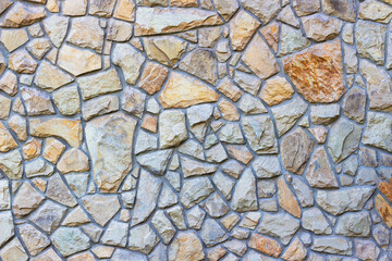 Texture of fence or stone wall made of irregularly shaped natural rocks in warm beige, yellow, gray tones. Perfect for backgrounds, architectural design, or construction themes