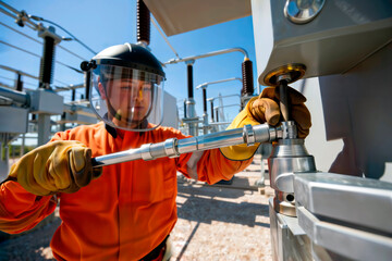 Electrical technician tightening high-voltage equipment outdoors.