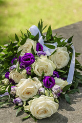 Beautiful funeral floral arrangement of white roses and blue eustomas at cemetery in Espoo, Finland. Beautiful funeral flowers on the stone. Blurred green background. Empty space for text.