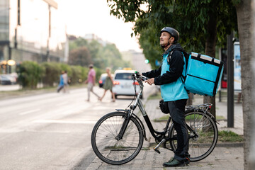 Delivery man with bicycle and backpack waiting in city traffic
