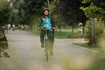 Obraz premium Delivery man riding bicycle in park delivering food order
