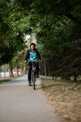 Naklejka premium Courier riding bicycle in city park delivering food with backpack