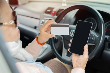 Rear view of elderly aged woman sitting in the car, looking at blank plastic card in hand