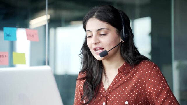 Young smiling female corporate operator in headset working in customer support service on helpline telesale talking using laptop in business office. Agent of call center advises client online Close up