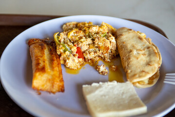 This is a top down studio shot of a fresh food meal consisting of eggs, tamal, cheese and stuffed tortilla on a plate.