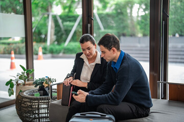 Business travelers sitting in hotel lobby discussing plans while checking information on a smartphone. Perfect for travel, hospitality, and corporate meeting concepts.
