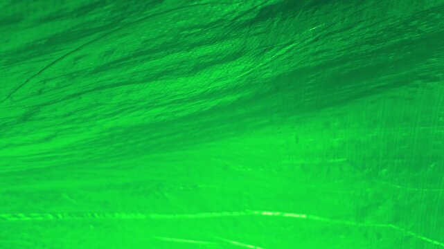 A bright green textured surface is visible. The lighting highlights the subtle ripples and irregularities in the material. It resembles a close-up of synthetic fabric, plastic sheeting, or tarpaulin.