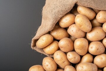 A burlap sack spilling fresh, earthy potatoes against a dark background, showcasing their smooth skin and natural texture.