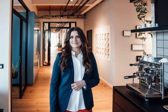 Businesswoman in business attire standing by coffee machine in modern office